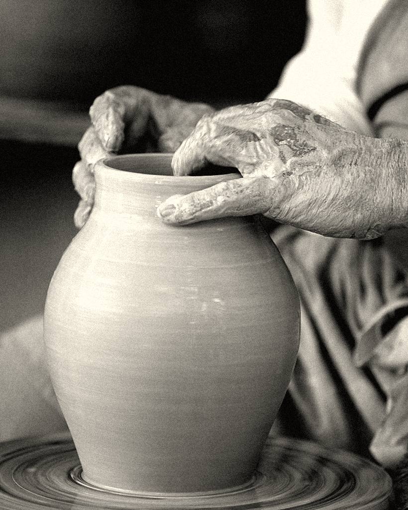 Hands shaping a pot on a potter's wheel.