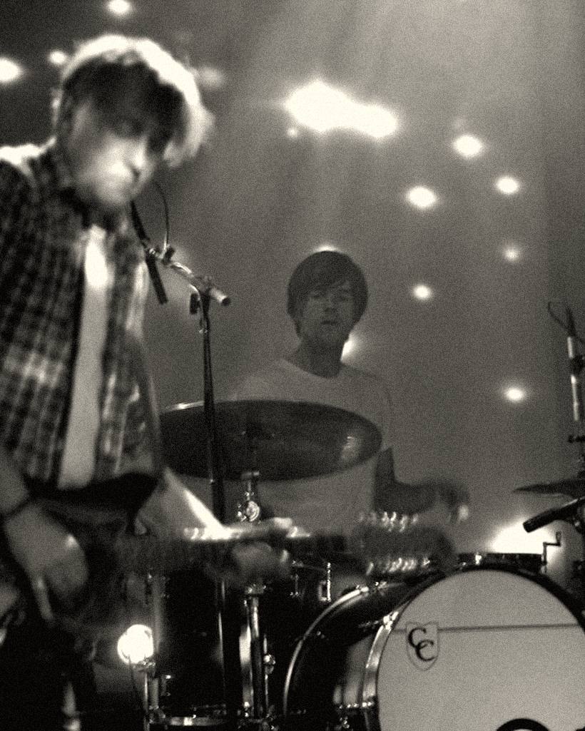 A drummer and a guitarist playing on a small stage.