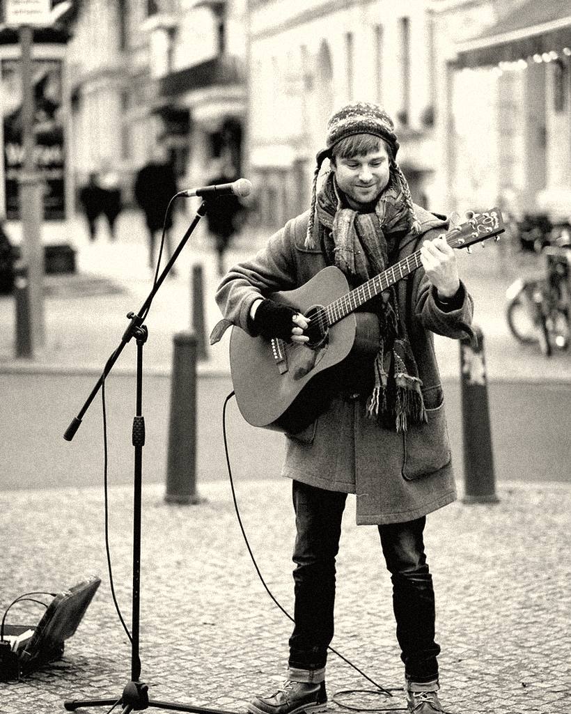 A busker playing an acoustic guitar on a cobbled street.