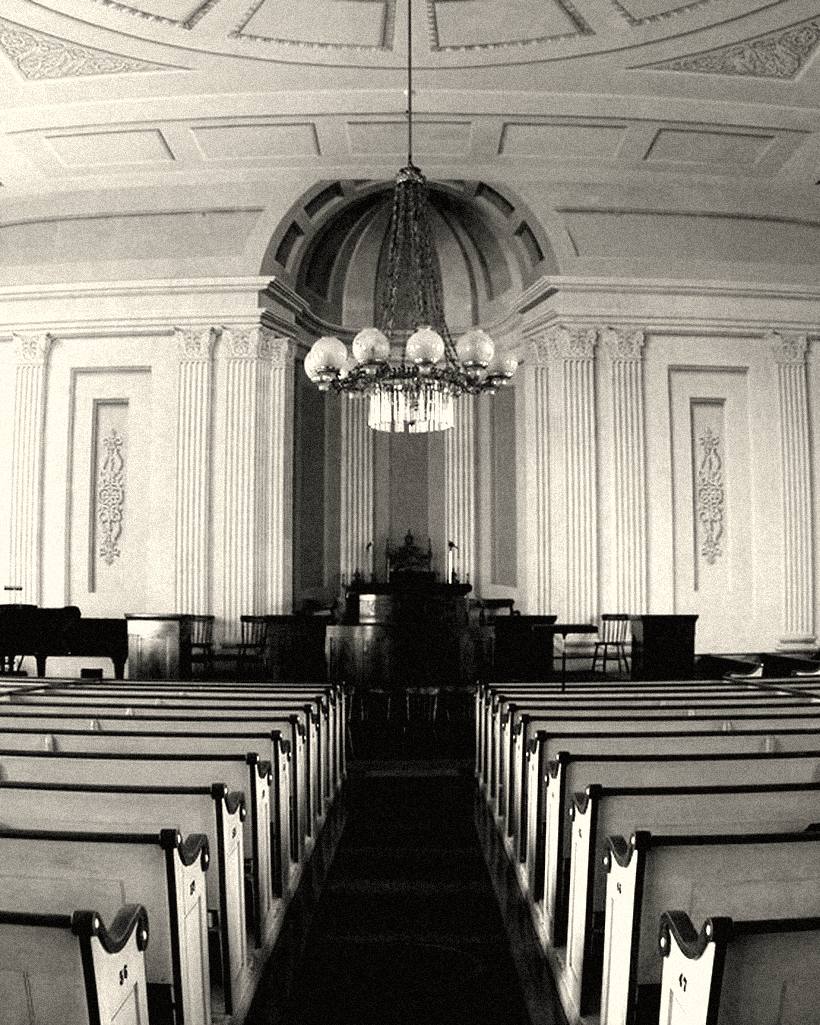 The inside of a church, rows of empty pews under a chandelier.