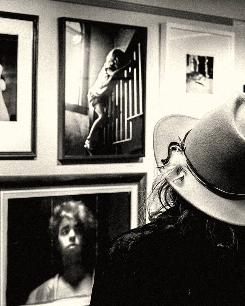 A visitor in a wide-brimmed hat looking at framed photographs on a gallery wall.