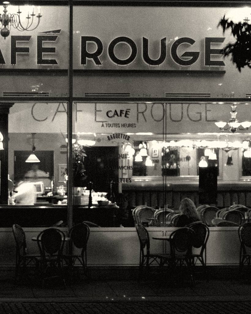 A cafe front at night, tables visible through the window.